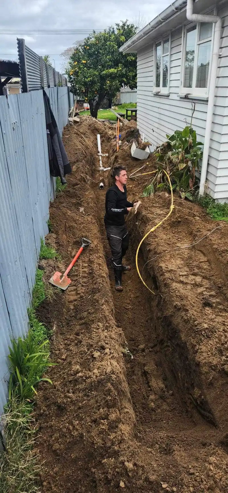 Plumber laying a new drain line in a trench along a boundary fence