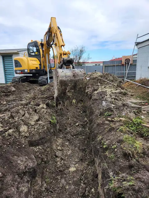 Digger excavating a trench for new drainage on a residential section