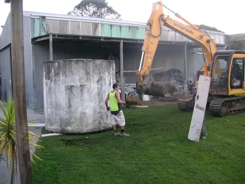 Old concrete tank being removed by excavator from a backyard