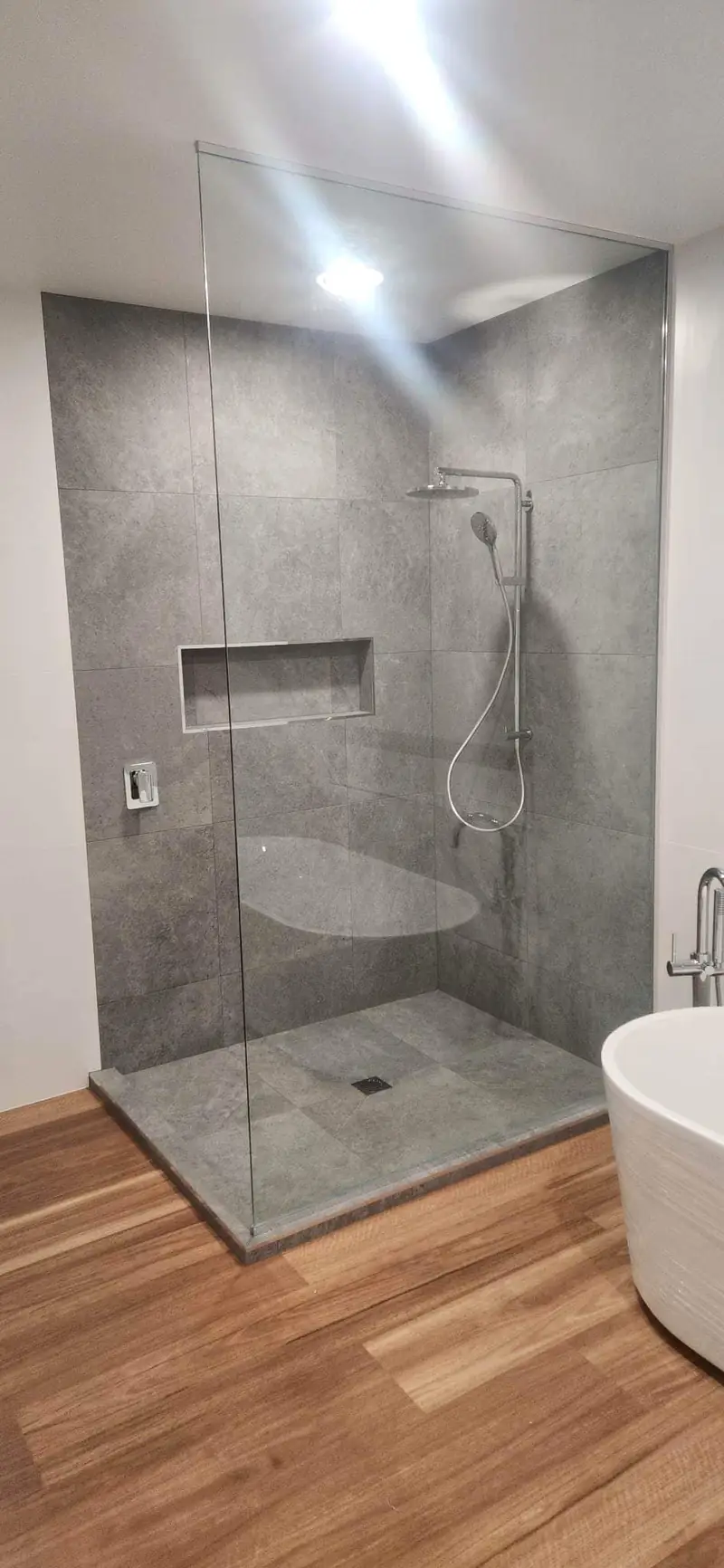 Tiled walk-in shower with glass screen and freestanding bath after a renovation