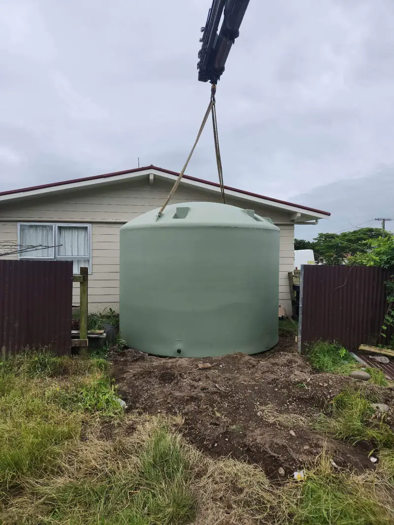 Crane lowering a new water tank into place beside a house